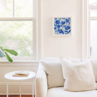 a cozy living room with a white sofa, a small round table, and a framed artwork of blue flowers on the wall.