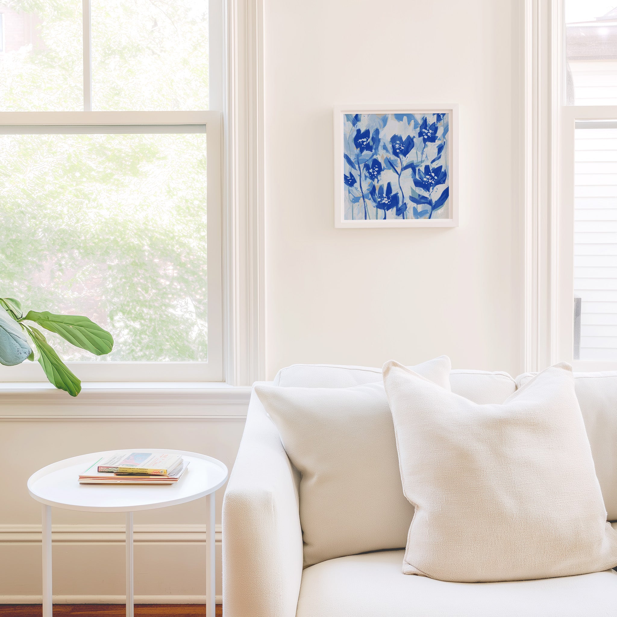 a cozy living room with a white sofa, a small round table, and a framed artwork of blue flowers on the wall.