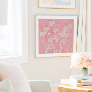 a cozy living room with a pink floral painting hanging on the wall, a vase of pink flowers on a table, and a white chair.