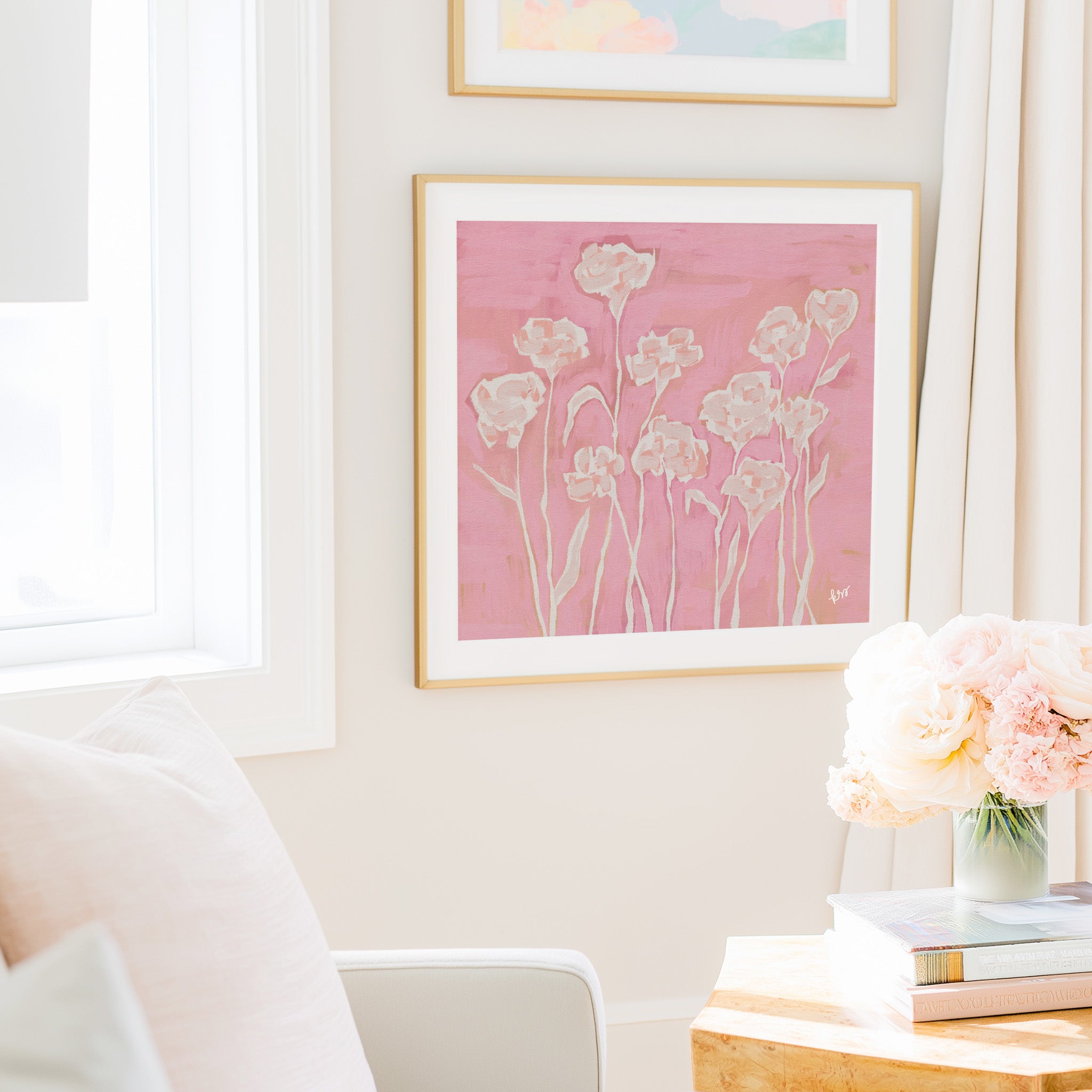 a cozy living room with a pink floral painting hanging on the wall, a vase of pink flowers on a table, and a white chair.