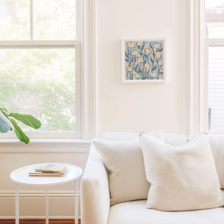 a cozy living room with a white sofa, a small white side table, and a framed artwork of flowers on the wall.