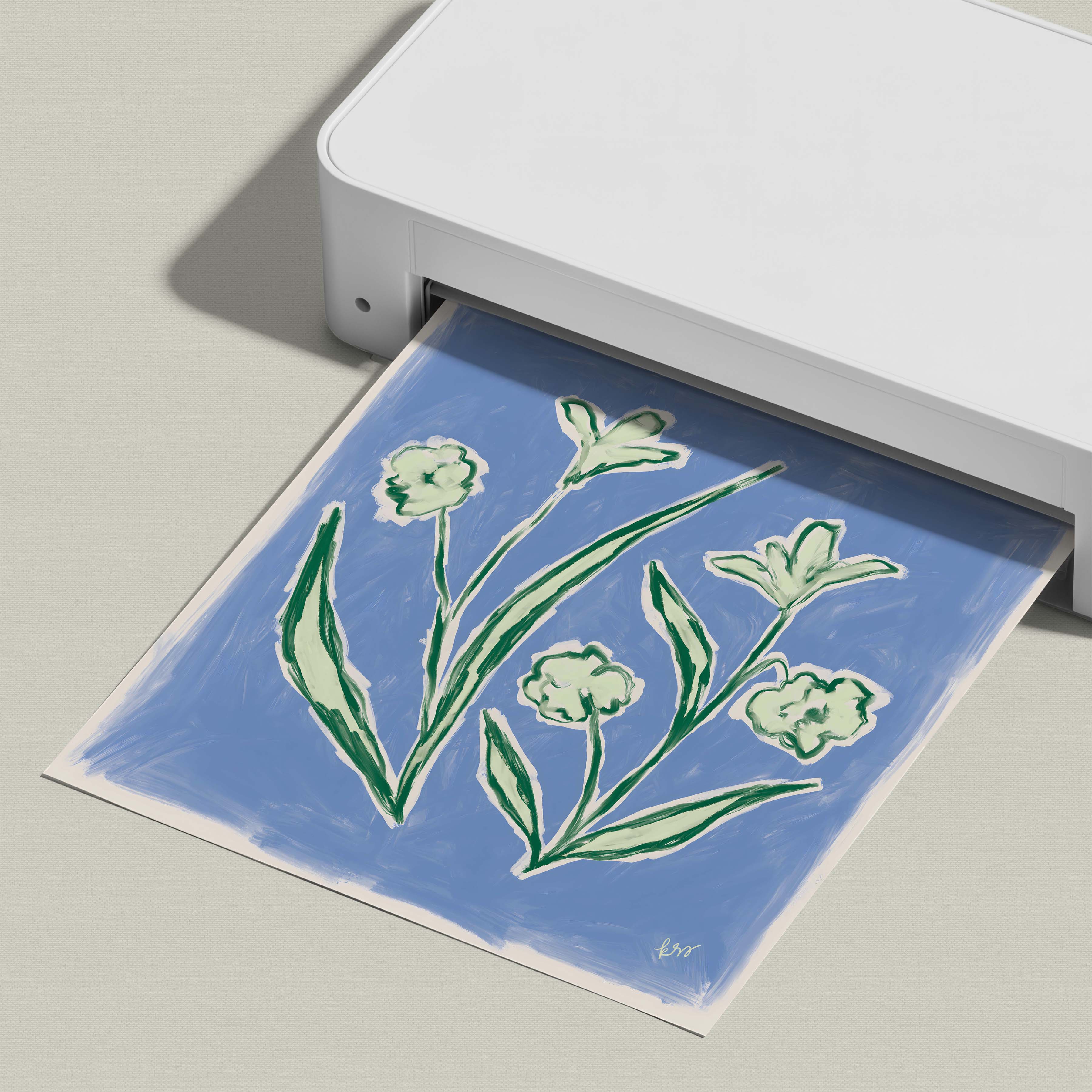 A white printer is printing a blue and green floral design on a piece of paper.
