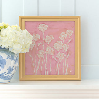 a framed painting of white flowers on a pink background, placed on a white shelf next to a blue and white vase filled with white hydrangeas.