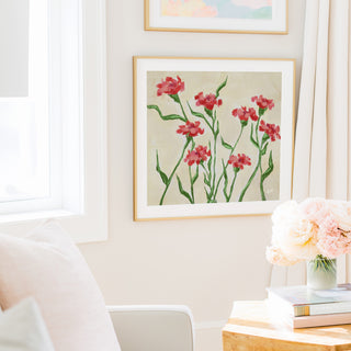 a cozy living room with a framed painting of red flowers hanging on the wall, a vase of pink flowers on a table, and a bookshelf filled with books.
