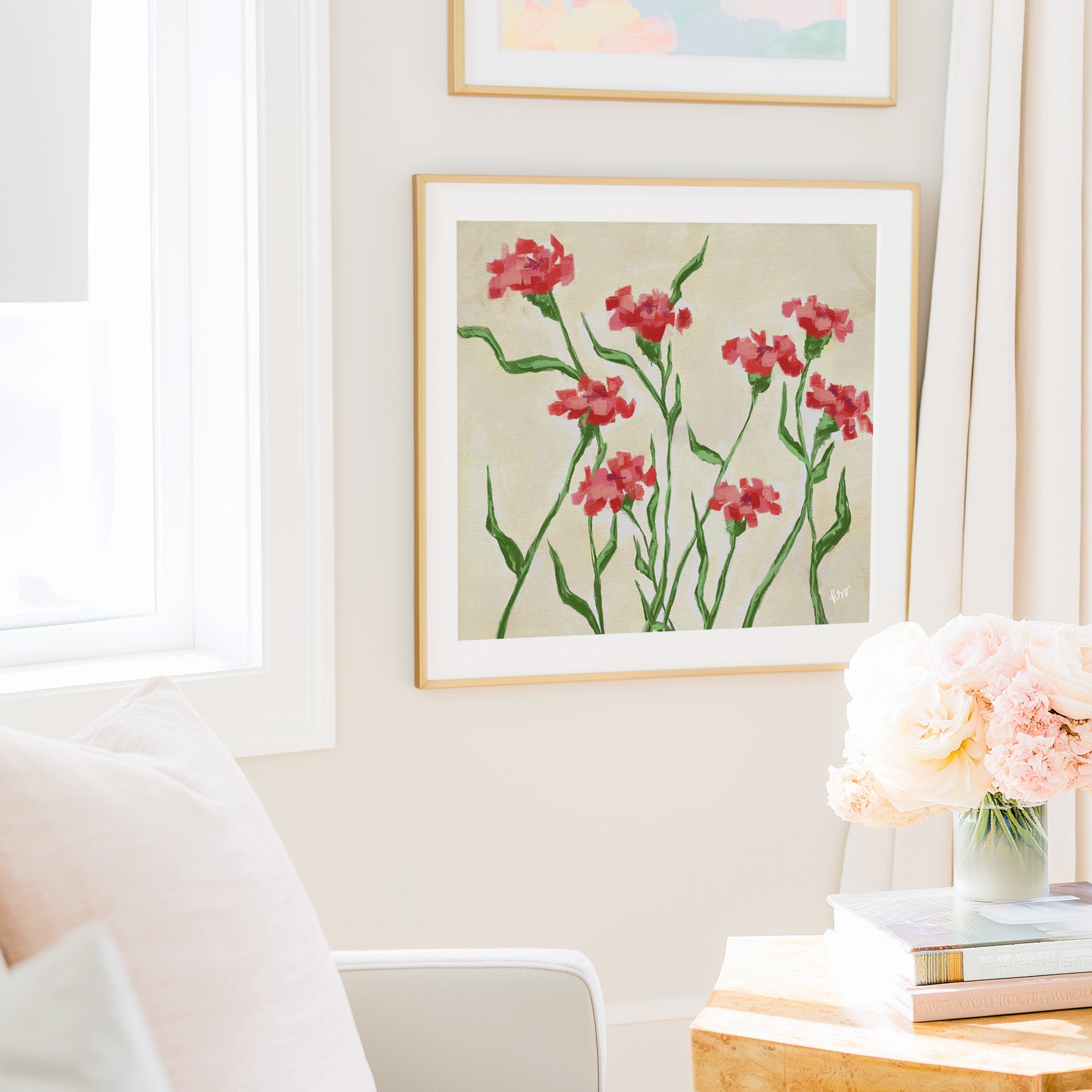 a cozy living room with a framed painting of red flowers hanging on the wall, a vase of pink flowers on a table, and a bookshelf filled with books.