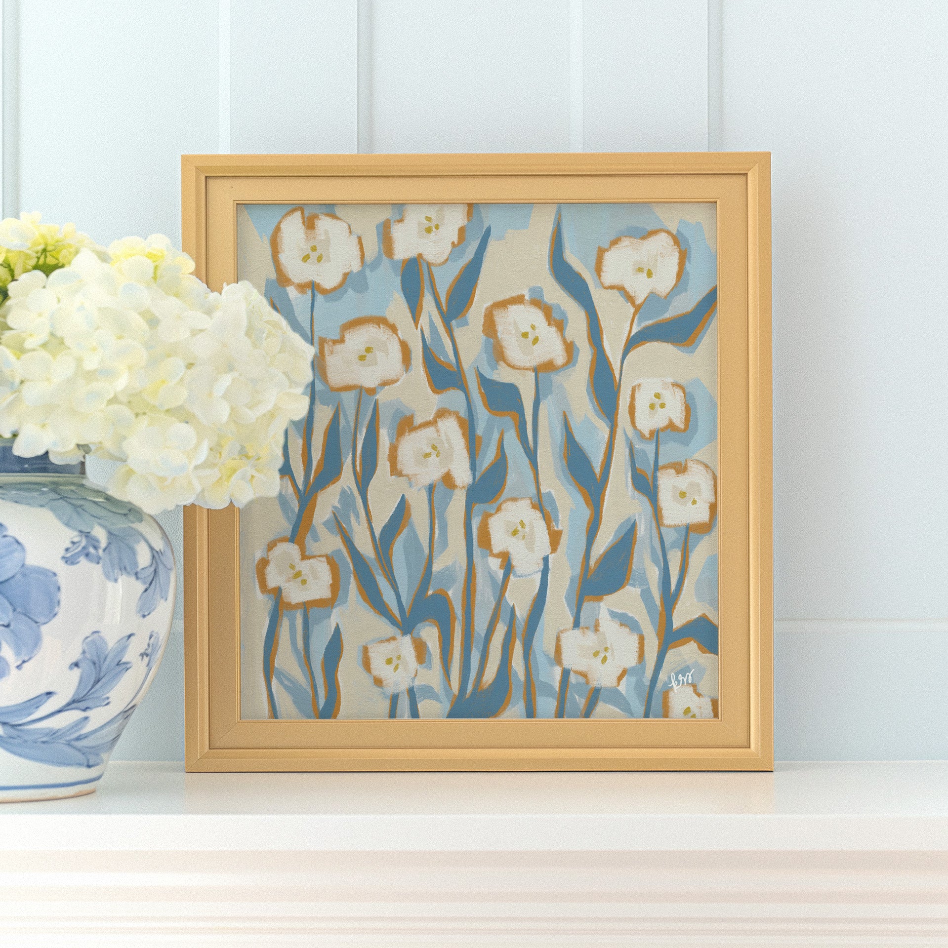 a framed painting of white flowers with blue and green accents, placed on a white shelf next to a blue and white vase filled with white hydrangeas.