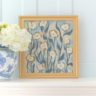a framed painting of white flowers with blue and green accents, placed on a white shelf next to a blue and white vase filled with white hydrangeas.