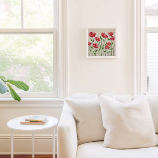 a cozy living room with a white sofa, a small round table, and a framed picture of red flowers on the wall.
