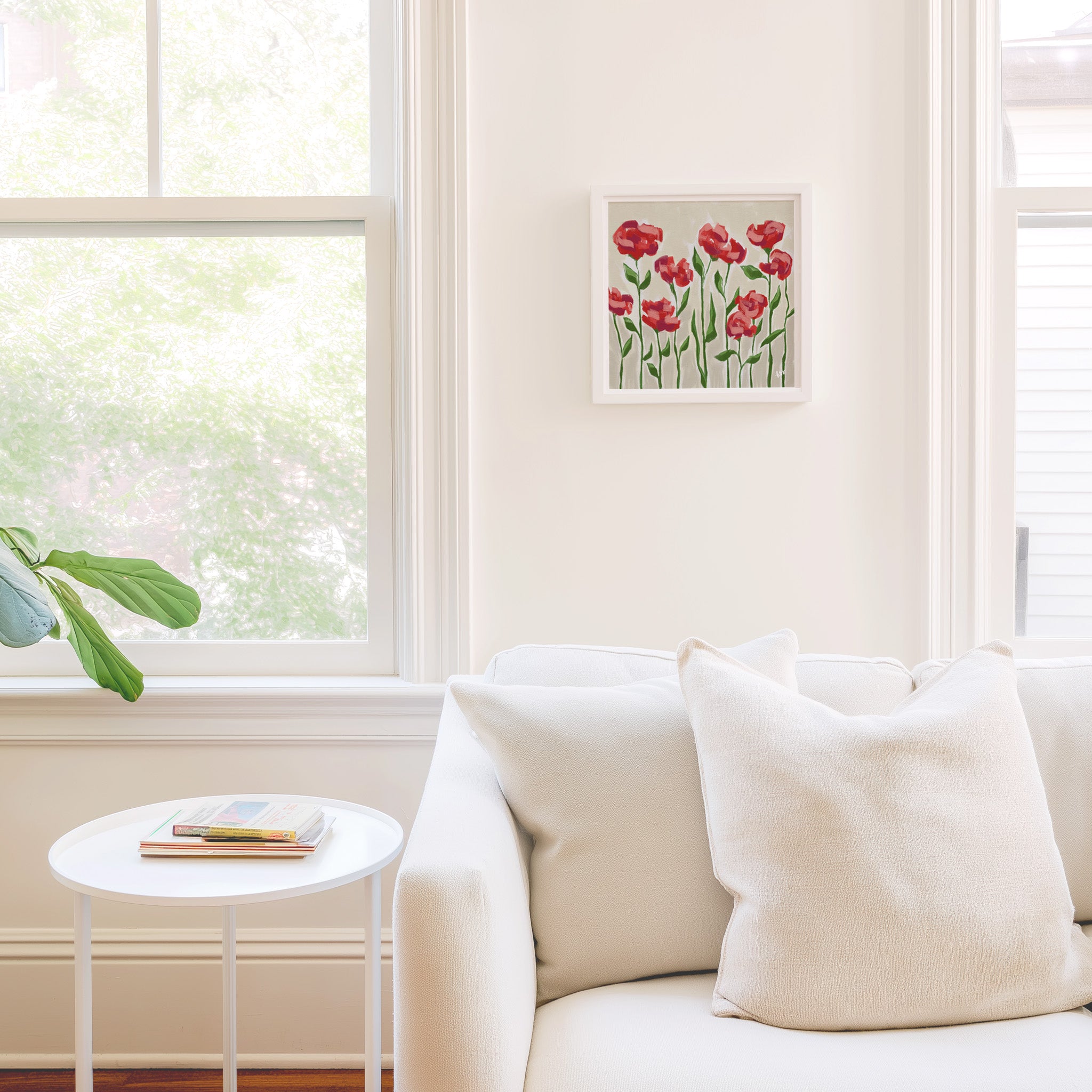 a cozy living room with a white sofa, a small round table, and a framed picture of red flowers on the wall.