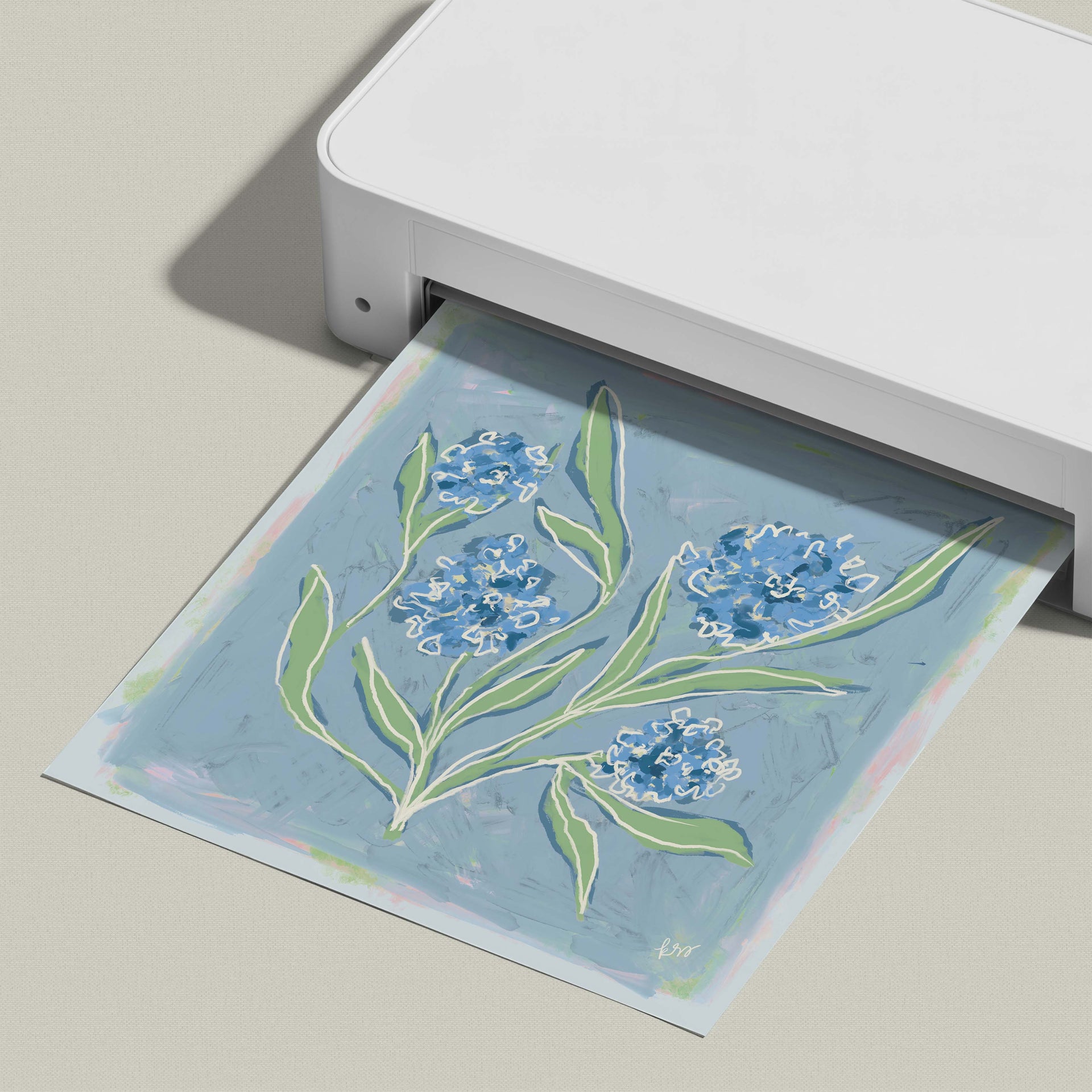 A white printer is printing a blue and green floral design onto a piece of paper.