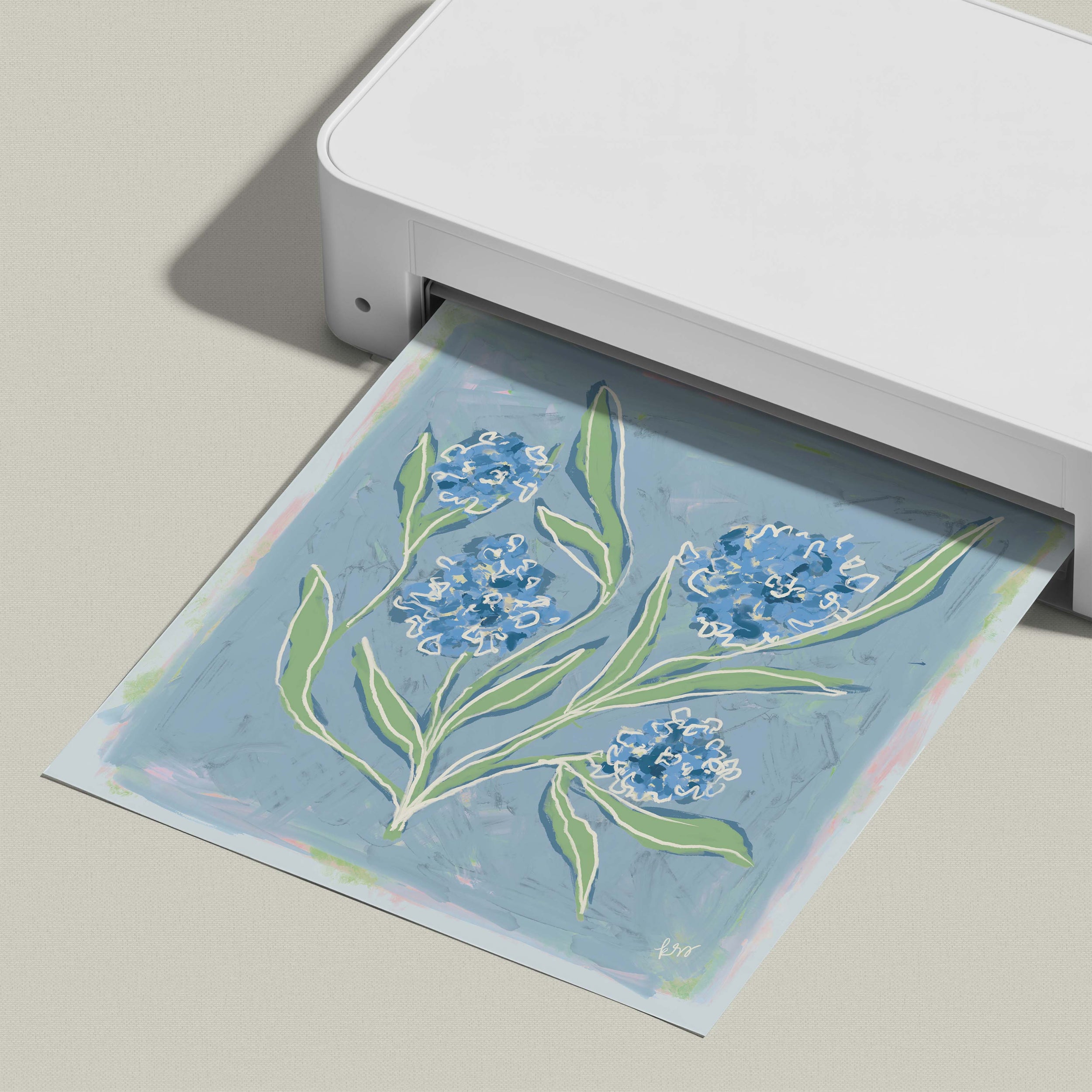A white printer is printing a blue and green floral design onto a piece of paper.