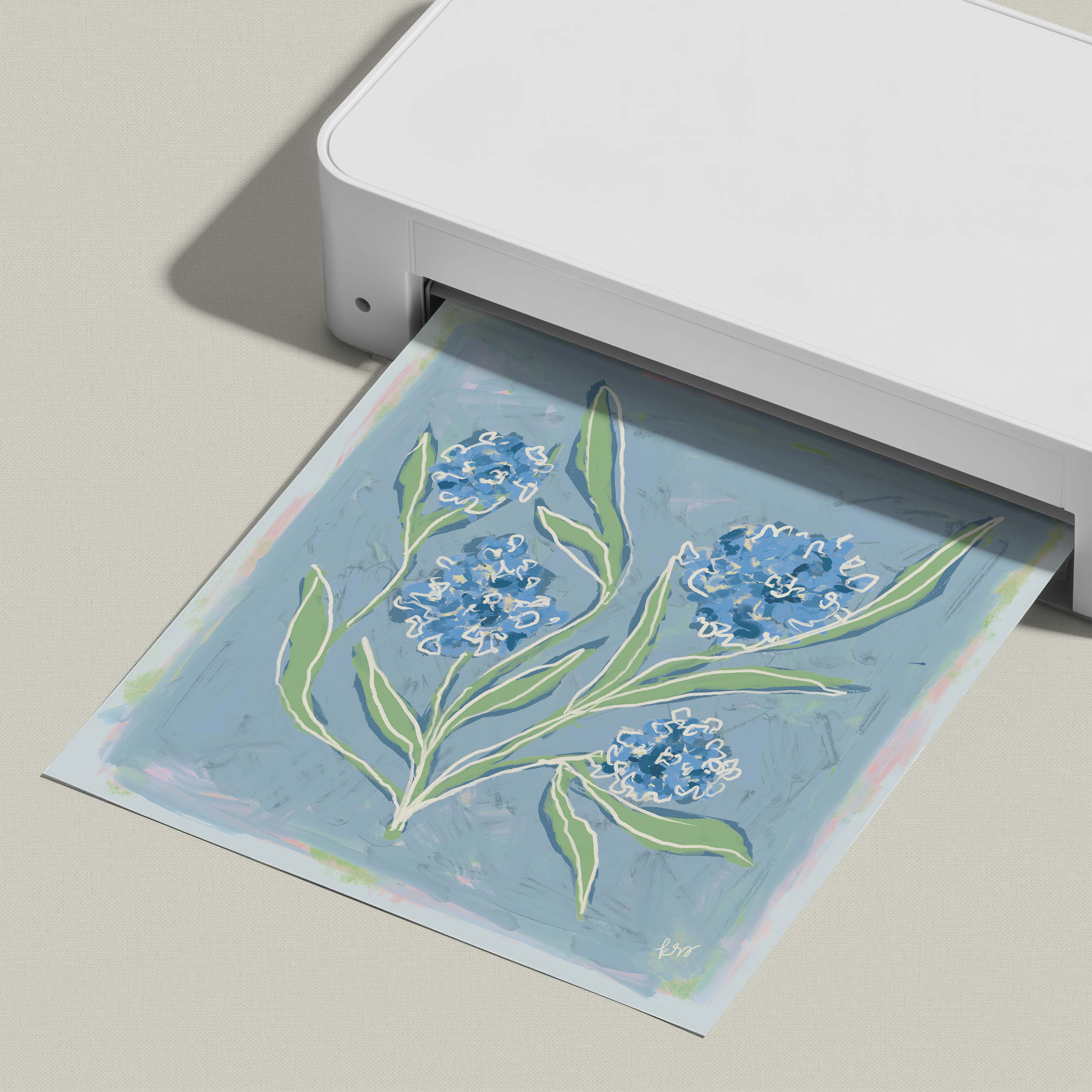 A white printer is printing a blue and green floral design onto a piece of paper.