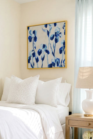 a serene bedroom scene with a bed adorned with white linens and a framed blue and white floral artwork hanging above it.