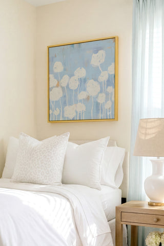 a serene bedroom scene with a bed adorned with white pillows and a blue and white floral painting hanging above it.