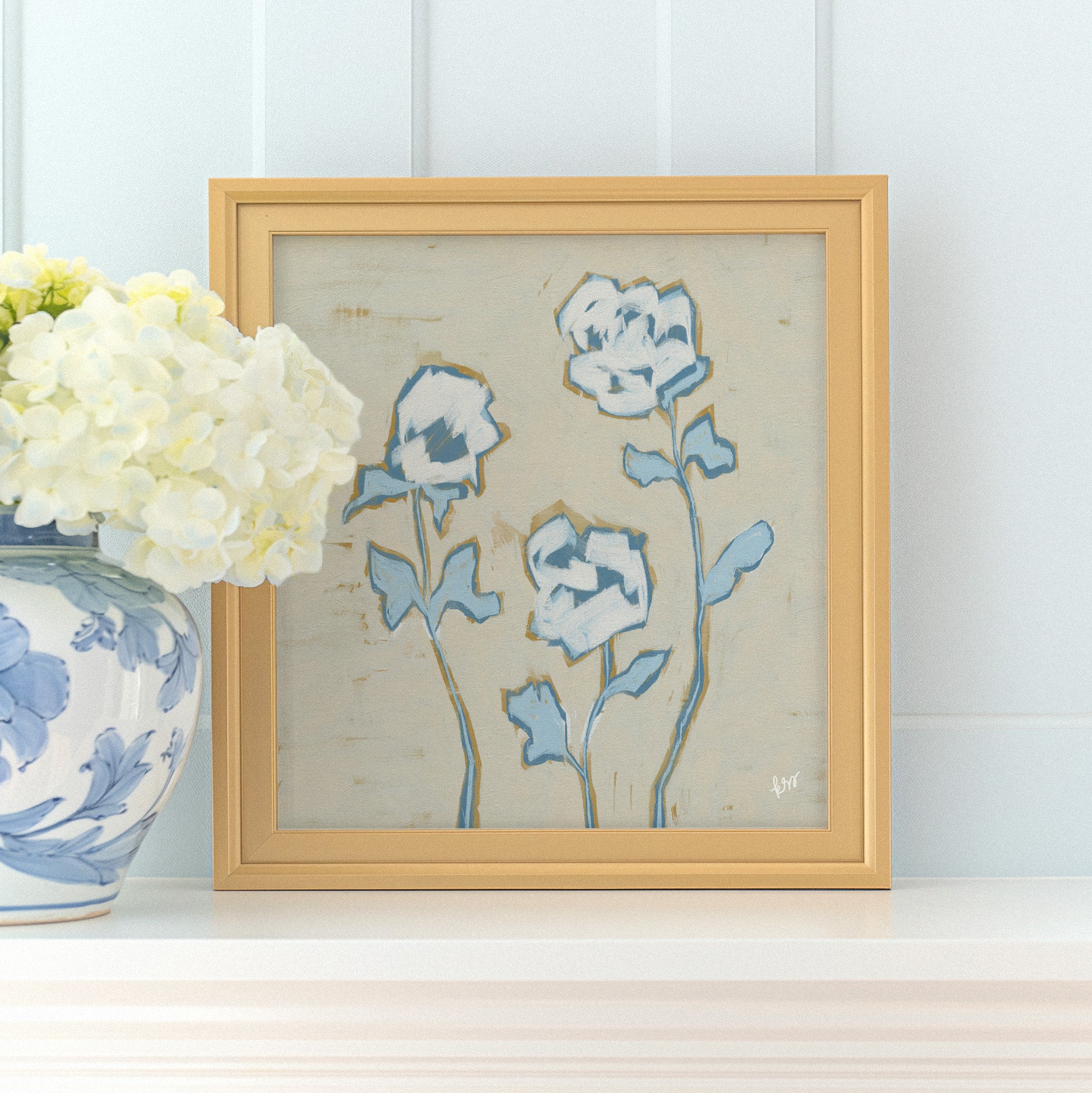 a framed painting of blue flowers on a white shelf, accompanied by a vase of white hydrangeas.