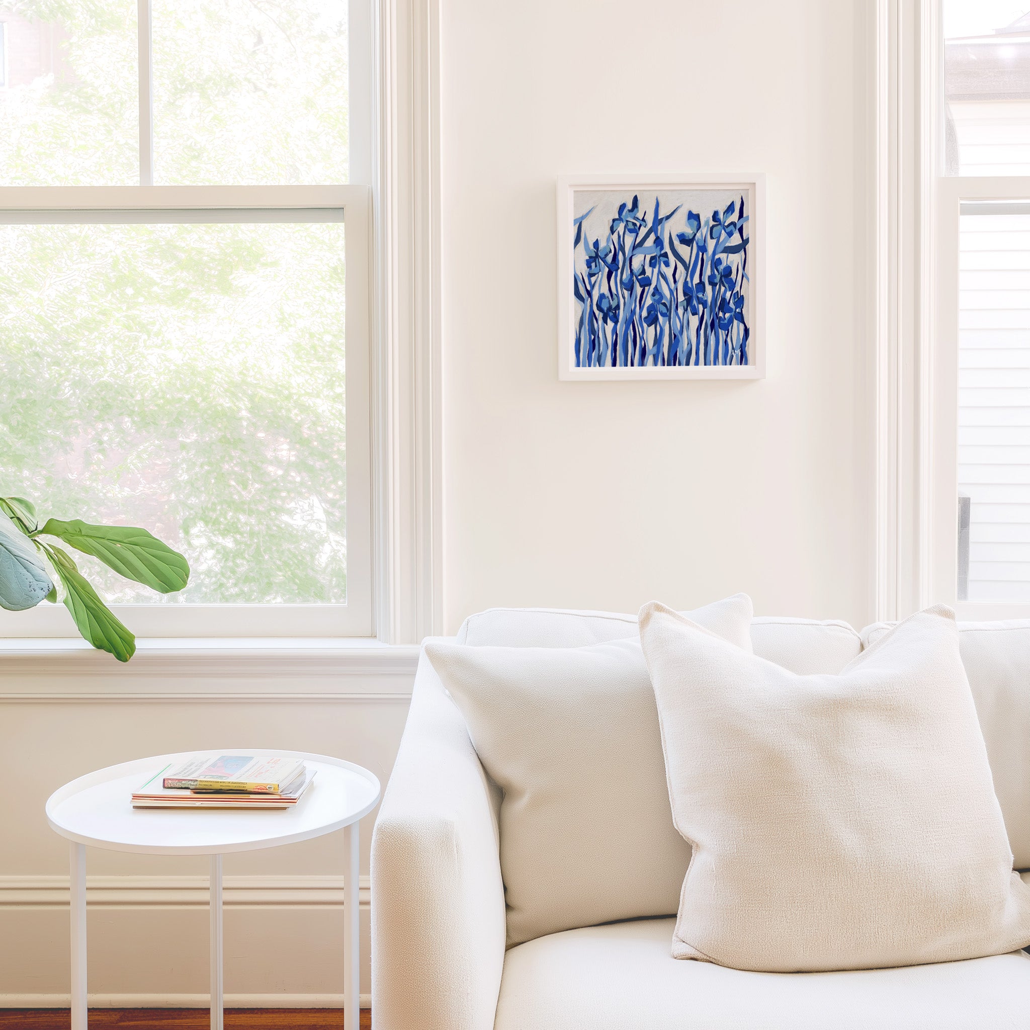 a cozy living room with a white sofa, a small round table, and a framed blue abstract painting hanging on the wall.