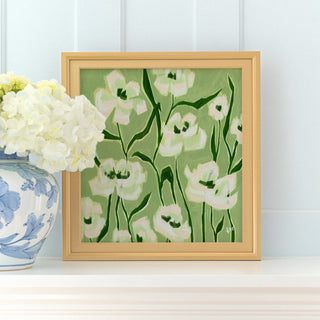 a framed painting of white flowers with green stems, placed on a white shelf next to a blue and white vase filled with white hydrangeas.