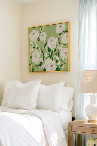 a serene bedroom scene with a bed adorned with white pillows and a white comforter, complemented by a framed floral artwork hanging above it.