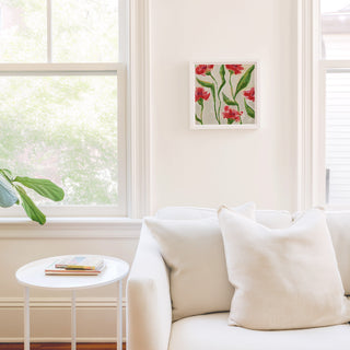 a cozy living room with a white sofa, a small round table, and a framed artwork of red flowers on the wall.