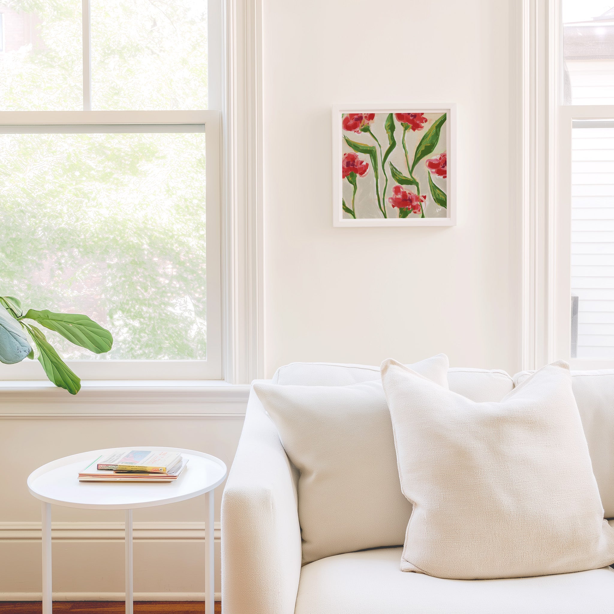a cozy living room with a white sofa, a small round table, and a framed artwork of red flowers on the wall.