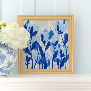 a framed painting of blue flowers on a white shelf, with a vase of white hydrangeas placed next to it.
