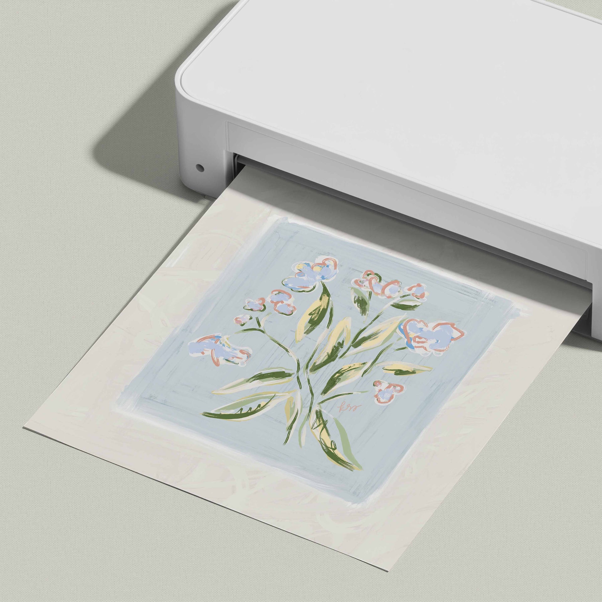 A white printer is printing a square-shaped image of a flower design on a light blue background.