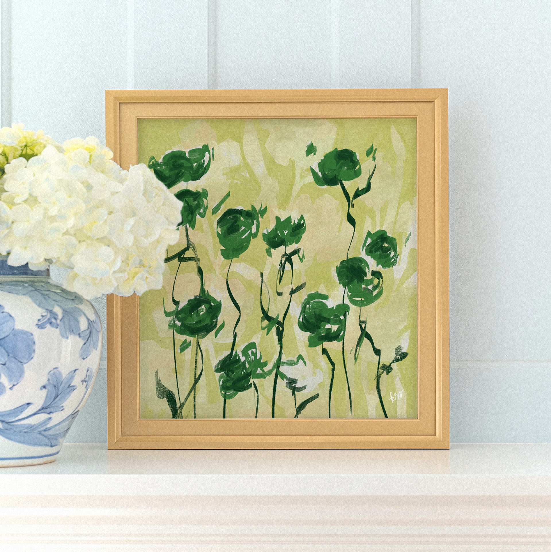 a framed painting of green flowers on a white shelf, with a vase of white hydrangeas placed next to it.