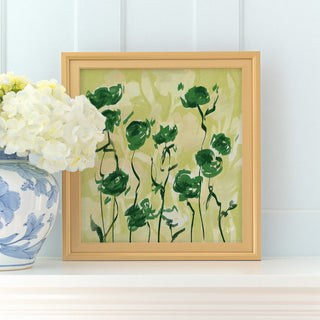a framed painting of green flowers on a white shelf, with a vase of white hydrangeas placed next to it.