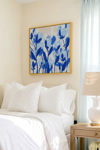 a serene bedroom scene with a bed adorned with white linens and a framed blue floral artwork hanging above it.