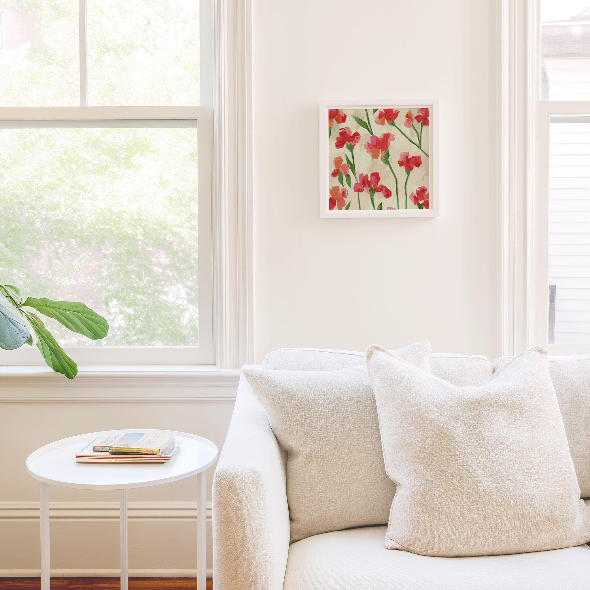 a cozy living room with a white sofa, a small round table, and a framed picture of red flowers on the wall.